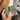 Anthurium Dark & Handsome - A hand holding two green leaves outdoors, with a blurred background showing a concrete path and brown ground.